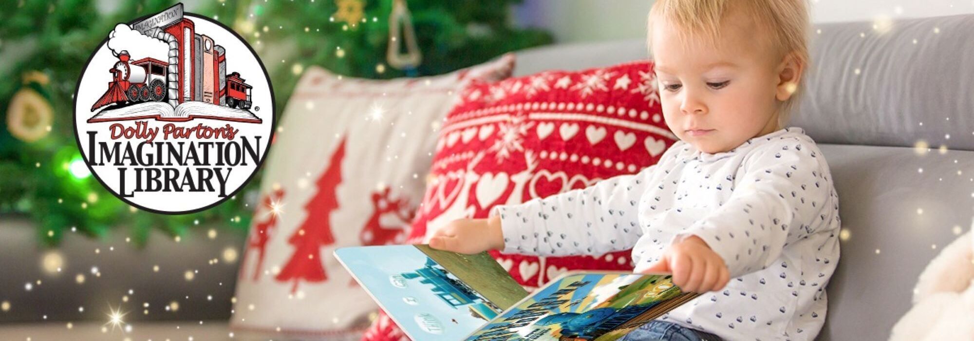 Toddler sitting on a couch reading a book.