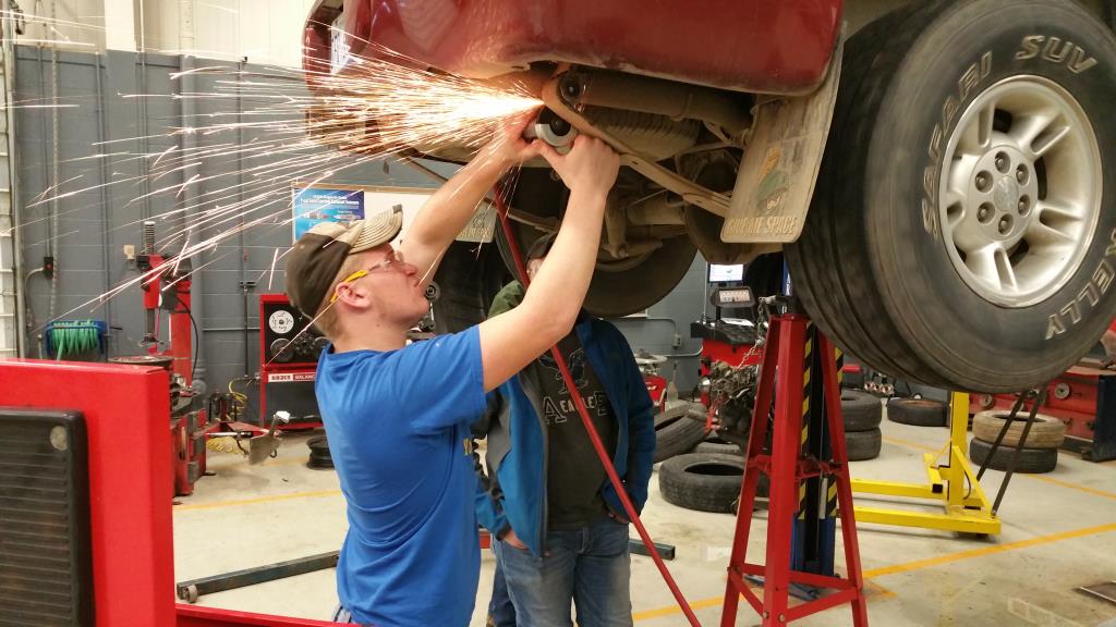 Students grinding a part on a car in auto class.