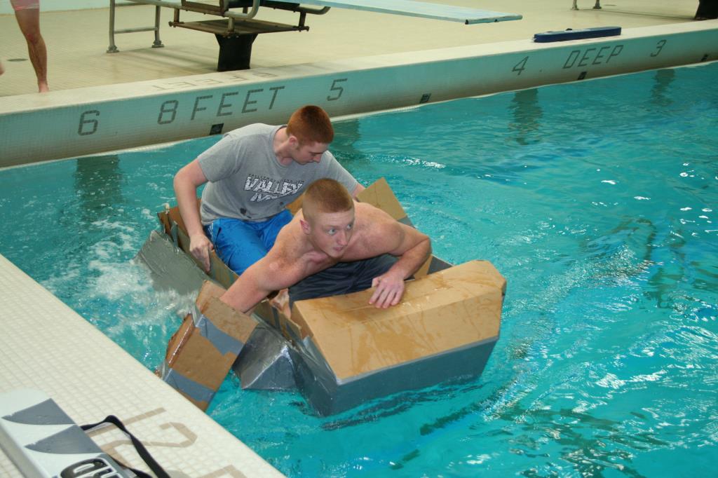 Two new students get into their cardboard boat to row back across the pool.