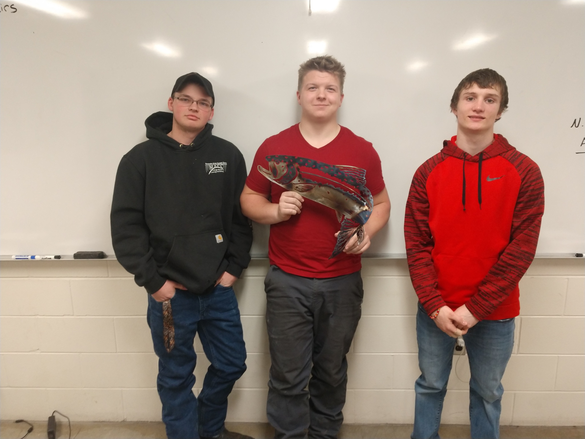 Welding students holding a fish sign that they cut out on the plasma table.